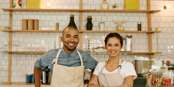Two smiling baristas wearing aprons in a cozy coffee shop.