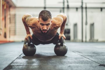 Man doing push-ups using kettlebells in a gym.