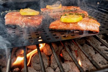 Grilled salmon fillets topped with lemon slices and herbs over hot charcoal.