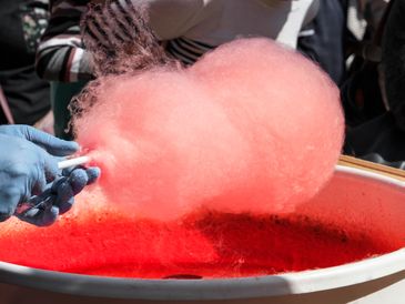 Hand holding pink cotton candy above red sugar mixture.