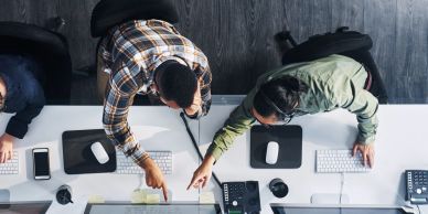 Two people pointing at a computer screen in an office.
