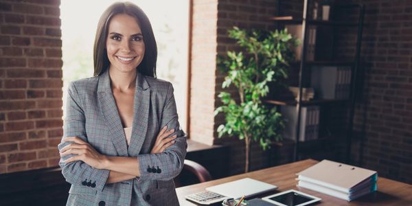 Confident woman standing in office with arms crossed and smiling.