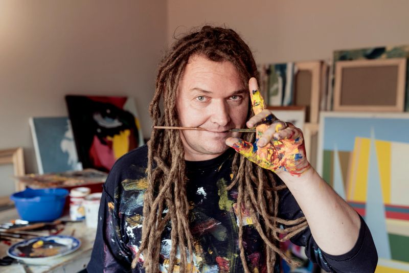 Photo of crazy mature male artist holding paintbrush in his mouth in his workplace art studio during the day.