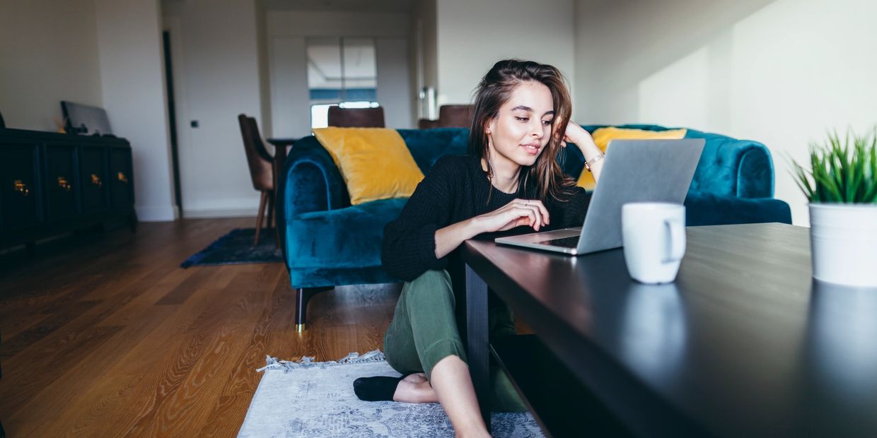 Young woman sitting on floor using laptop in cozy living room.