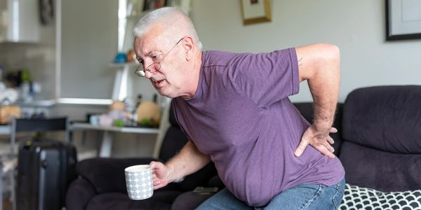 Man with sciatica struggling to stand from chair needing chiropractic care in Pymble