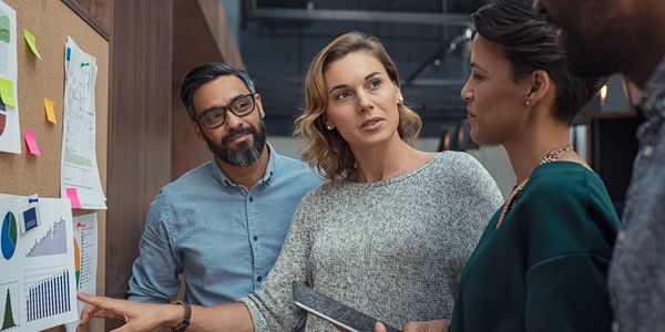 A team discussing charts and data on a bulletin board in an office.