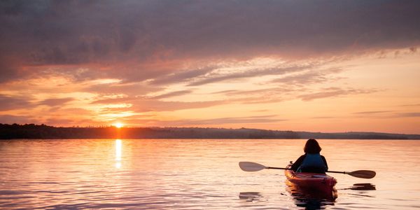 Person kayaking on calm water during a colorful sunset.