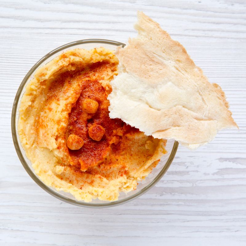 Bowl of Hummus with spices and pita bread on a white wooden table, overhead view. Closeup.