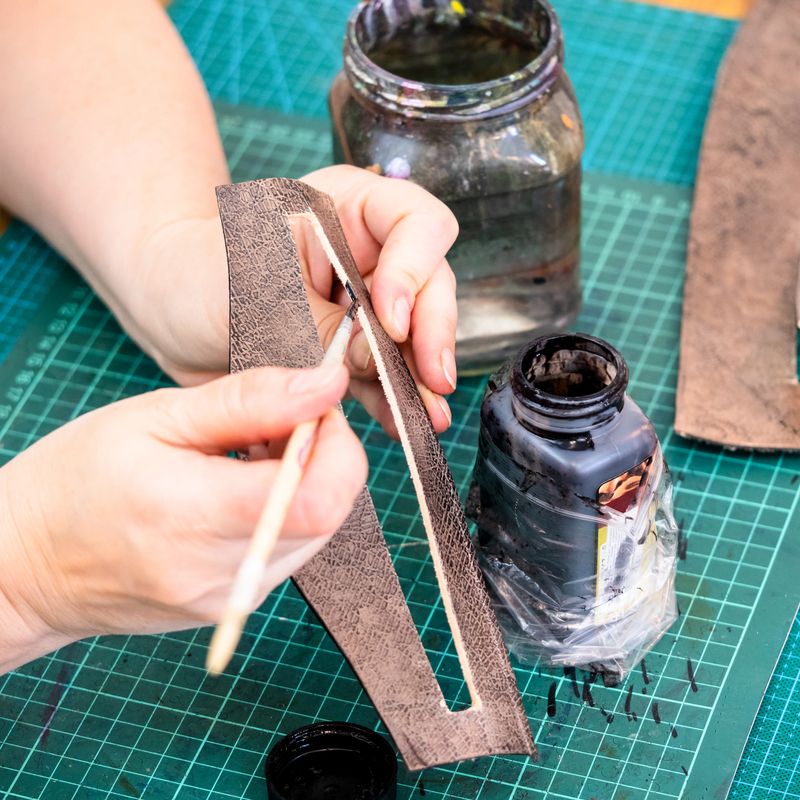 workshop of making the carved leather bag - craftsman tones the edges of the carved leather item for a handbag