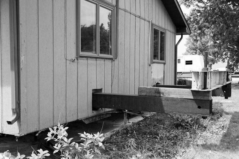 A house is being moved to a new location and will be placed on a new concrete slab.  The entire bottom four feet of the interior has been dismantled and holes cut through the siding to allow for the steel support beams. This image shows the house jacked up and steel beams through the siding.