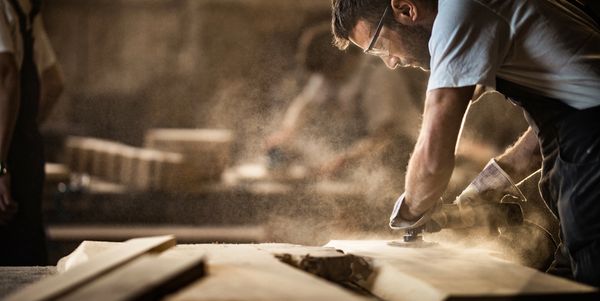 A craftsman shaping wood with a power tool in a workshop.