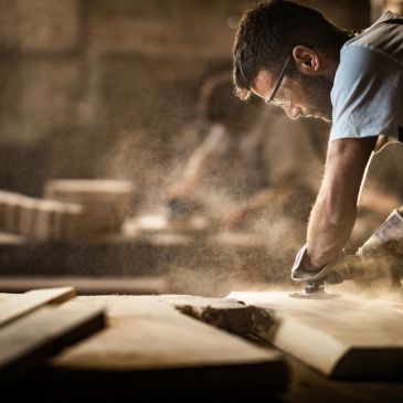 Carpenter working on wood in a workshop with dust particles.