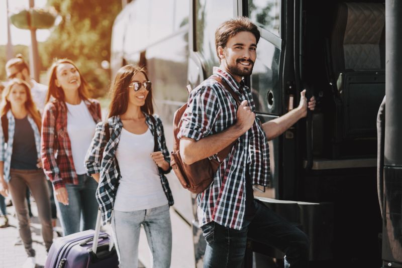Group of Young People Boarding on Travel Bus. Happy Travelers Standing in Queue Holding Luggage Waiting their turn to Enter Bus. Traveling, Tourism and People Concept. Summer Vacation