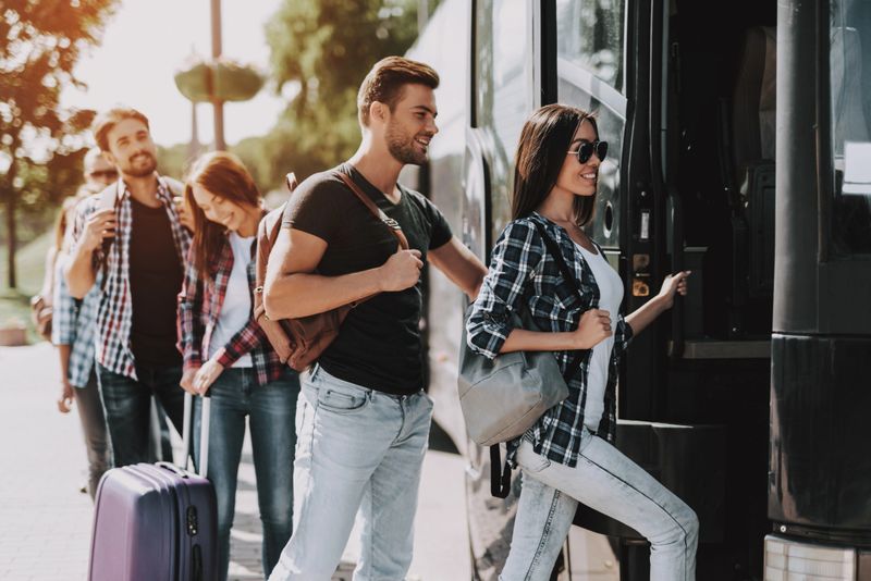 Group of Young People Boarding on Travel Bus. Happy Travelers Standing in Queue Holding Luggage Waiting their turn to Enter Bus. Traveling, Tourism and People Concept. Summer Vacation