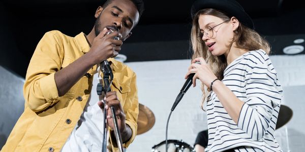 Two musicians rehearse with microphones in a studio setting.
