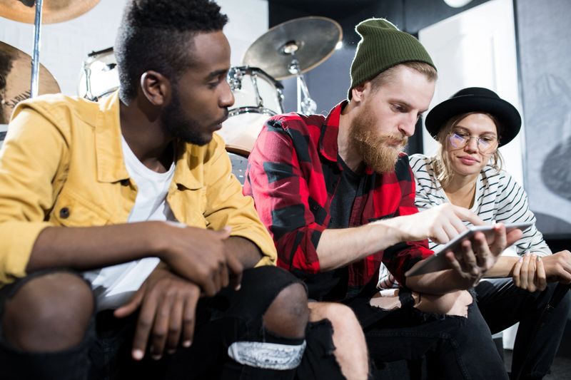 Multi-ethnic group of musicians using digital tablet while chilling in rehearsal studio