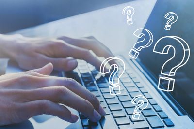 Hands typing on a laptop keyboard surrounded by floating question marks.