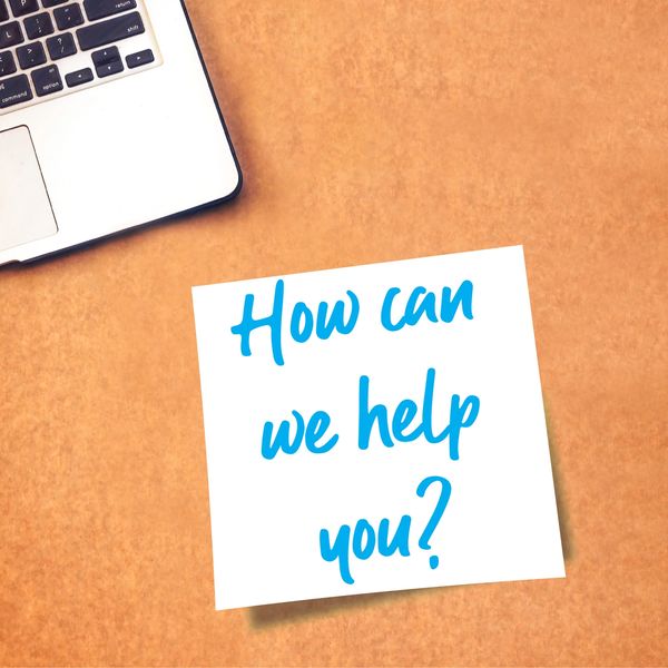 Sticky note on desk asks, 'How can we help you?' next to laptop.
