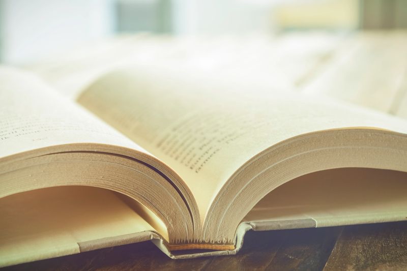 Beautiful high key closeup of an open book with white pages on a wooden table. Reading and literacy concept.