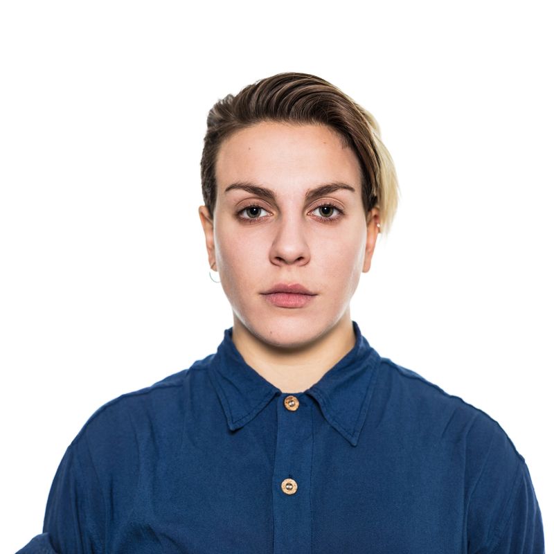 Close-up of serious woman with short blond hair. Portrait of young female is wearing blue shirt. She is against white background.