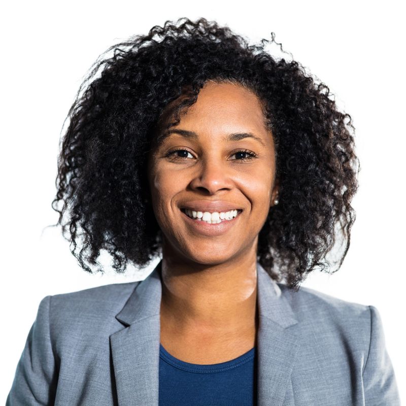 Portrait of smiling mid adult woman. Close-up of female with afro hair is in blazer. She is against white background.