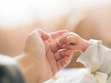 An adult hand gently holding a baby's tiny fist.