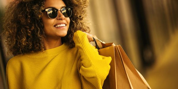 Smiling woman in yellow sweater holding shopping bags.