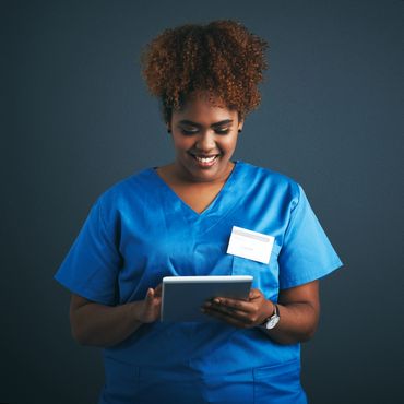 Smiling nurse in blue scrubs using a tablet.