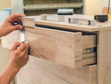 Person measuring and marking a wooden drawer front for handle installation.
