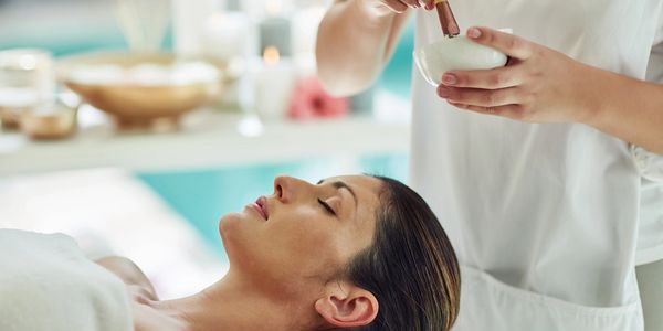 A woman relaxes while receiving a facial treatment at a spa.