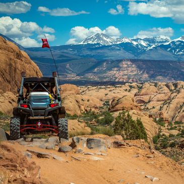 Off-road vehicle exploring rocky desert terrain with snow-capped mountains in the distance.