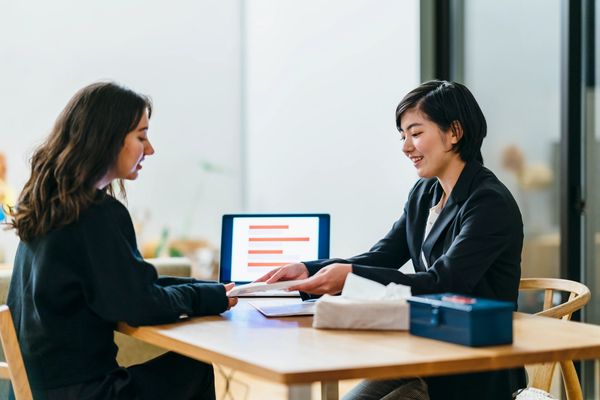 The image shows two women seated at a wooden table