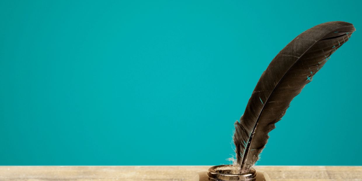 Black feather quill in ink bottle on wooden surface.