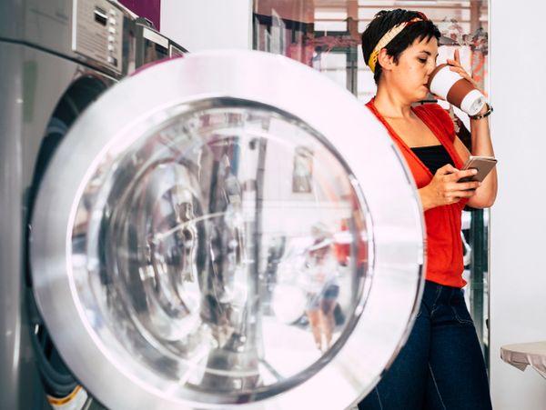 Woman sipping coffee while checking her phone at a laundromat.
