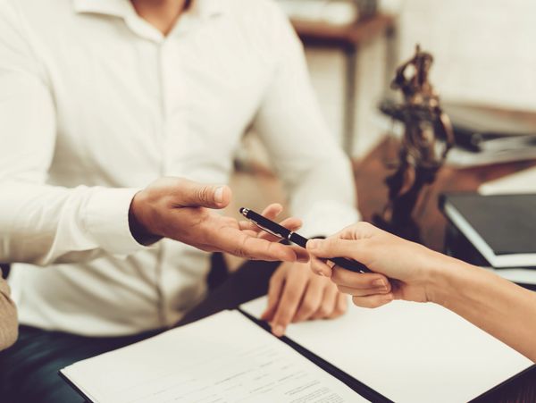 A person handing a pen to another over a document.