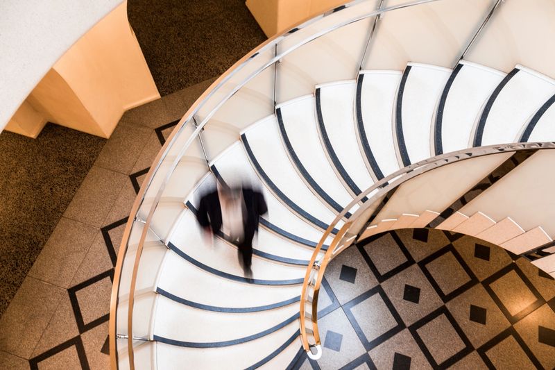 Overhead view depicting blurred motion of a business person (we cannot tell if it is a man or a woman) walking down a spiral staircase. The person is completely blurred, and the slow shutter speed makes it appear as though he is moving fast. Horizontal color image with room for copy space. Image taken at City Hall in London, which is a publicly owned building that is accessible to the general public without any photographic restrictions.