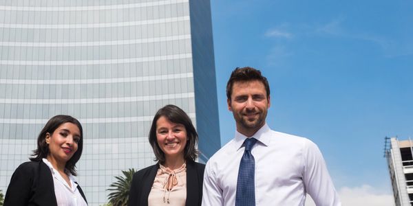 Three business professionals standing confidently outdoors against a skyscraper.