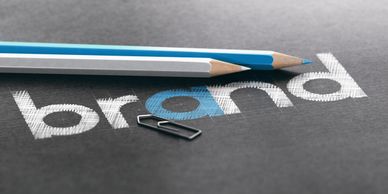 Two pencils and a paperclip on a blueprint with the word 'brand'.