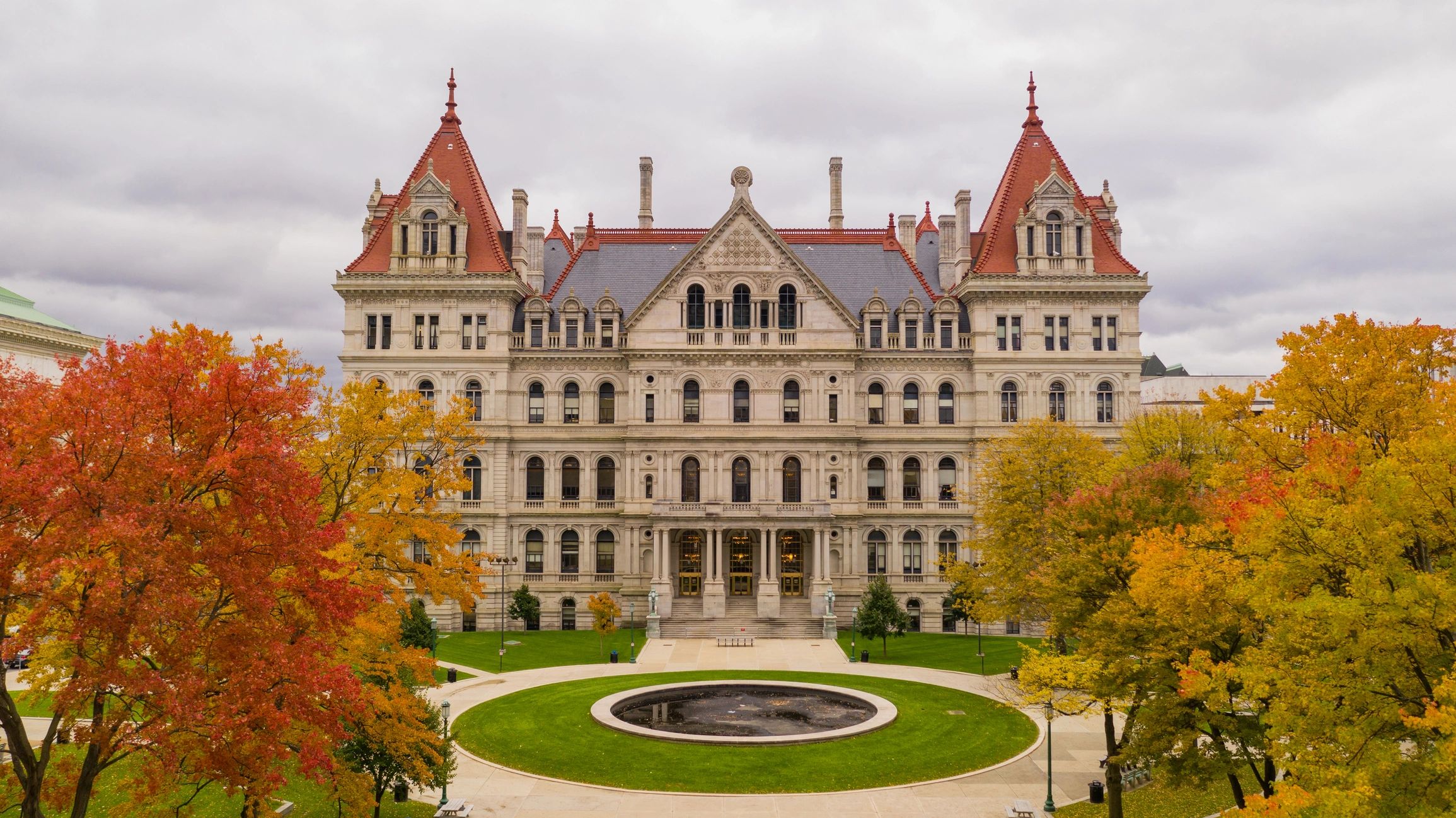 Historic government building with autumn trees and cloudy sky.