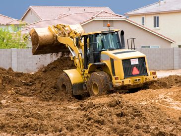 Bulldozer moving muddy earth in front of houses.