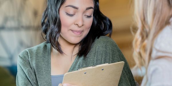 Woman shyly holding a clipboard during a conversation.