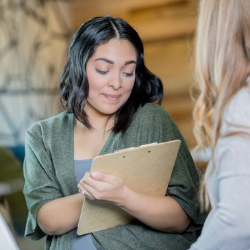Woman shyly holding a clipboard during a conversation.