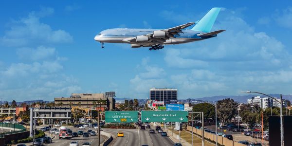 Large airplane flying above a busy highway in a city.