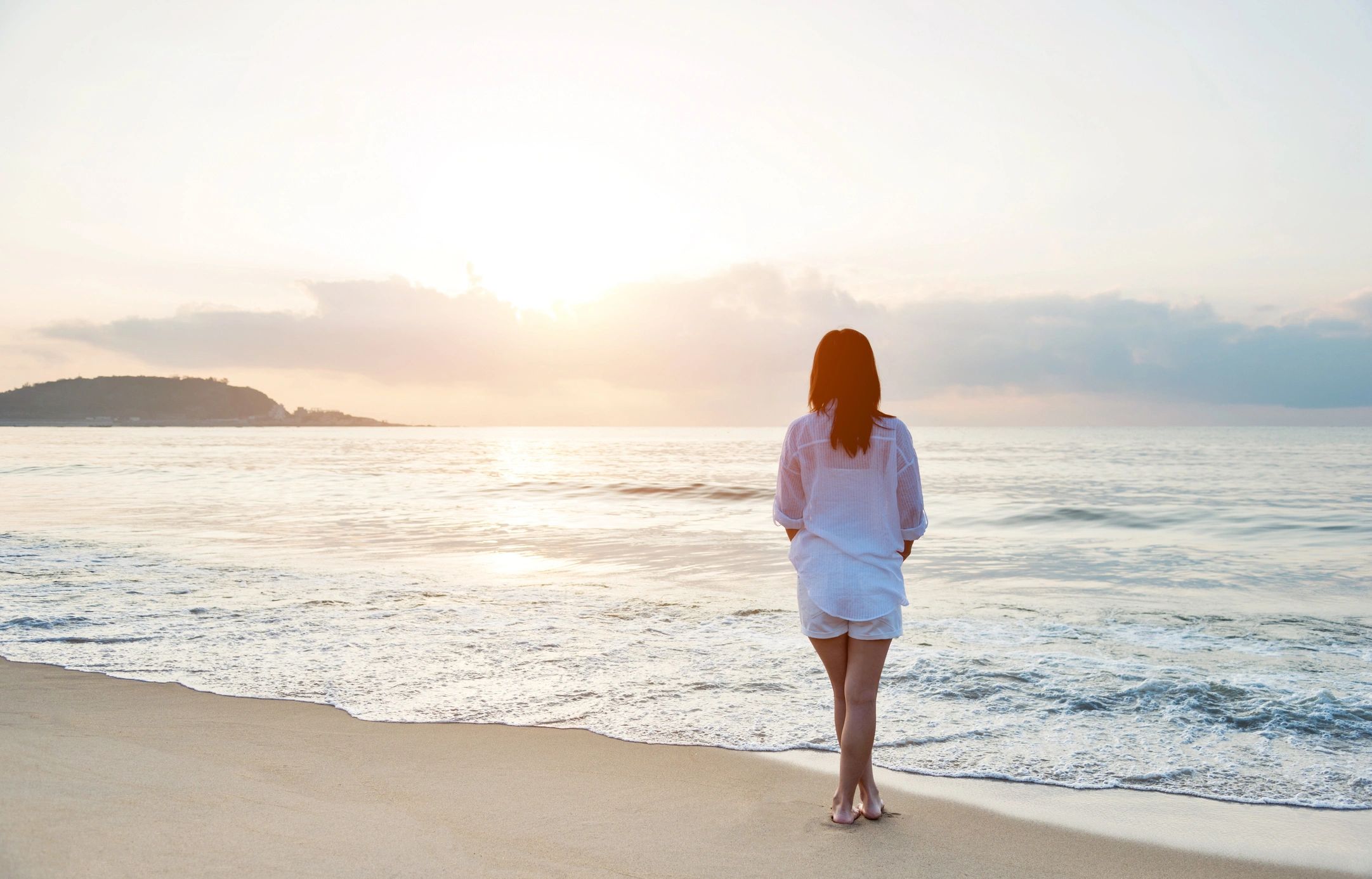 Woman standing on the beach looking at the sunrise.