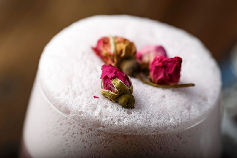 cocktail with high foam and with roses in a glass on a black background. romantic drink