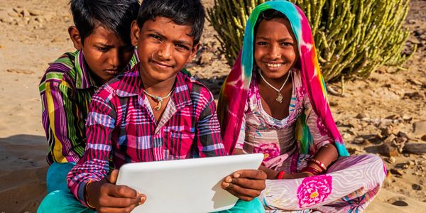 Three children in colorful clothes using a tablet outdoors.