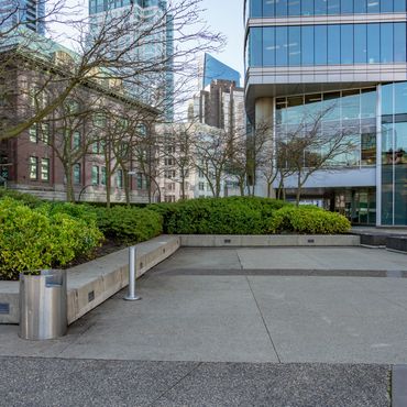 Urban plaza with benches and trees amidst tall buildings.