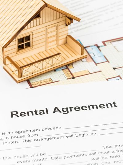 Two people shaking hands with a small wooden house between them, symbolizing a real estate deal.