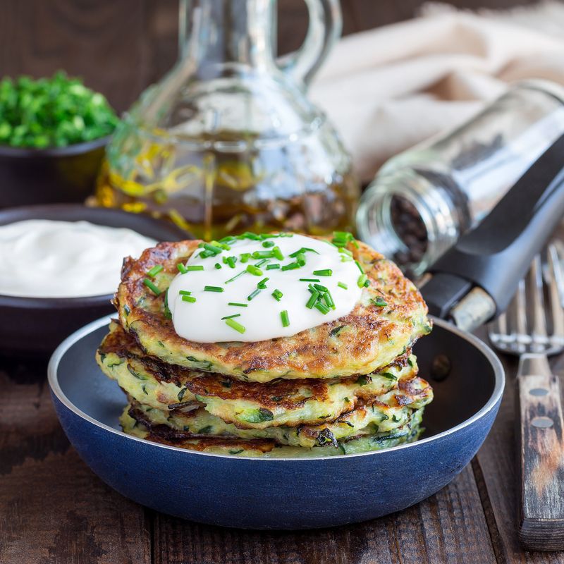 Vegetarian zucchini fritters or pancakes, served with greek yogurt and green onion, in a little pan, square format
