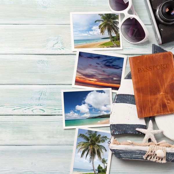 Travel essentials and vacation photos on a light wooden surface.